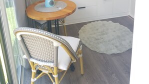 A compact kitchen with white cabinets, a microwave, a kettle, and a small sink. There is a round wooden table with a chair, a white rug, and a window with curtains. - QUIET COMFY PRIVATE TINY HOME (Caboolture)