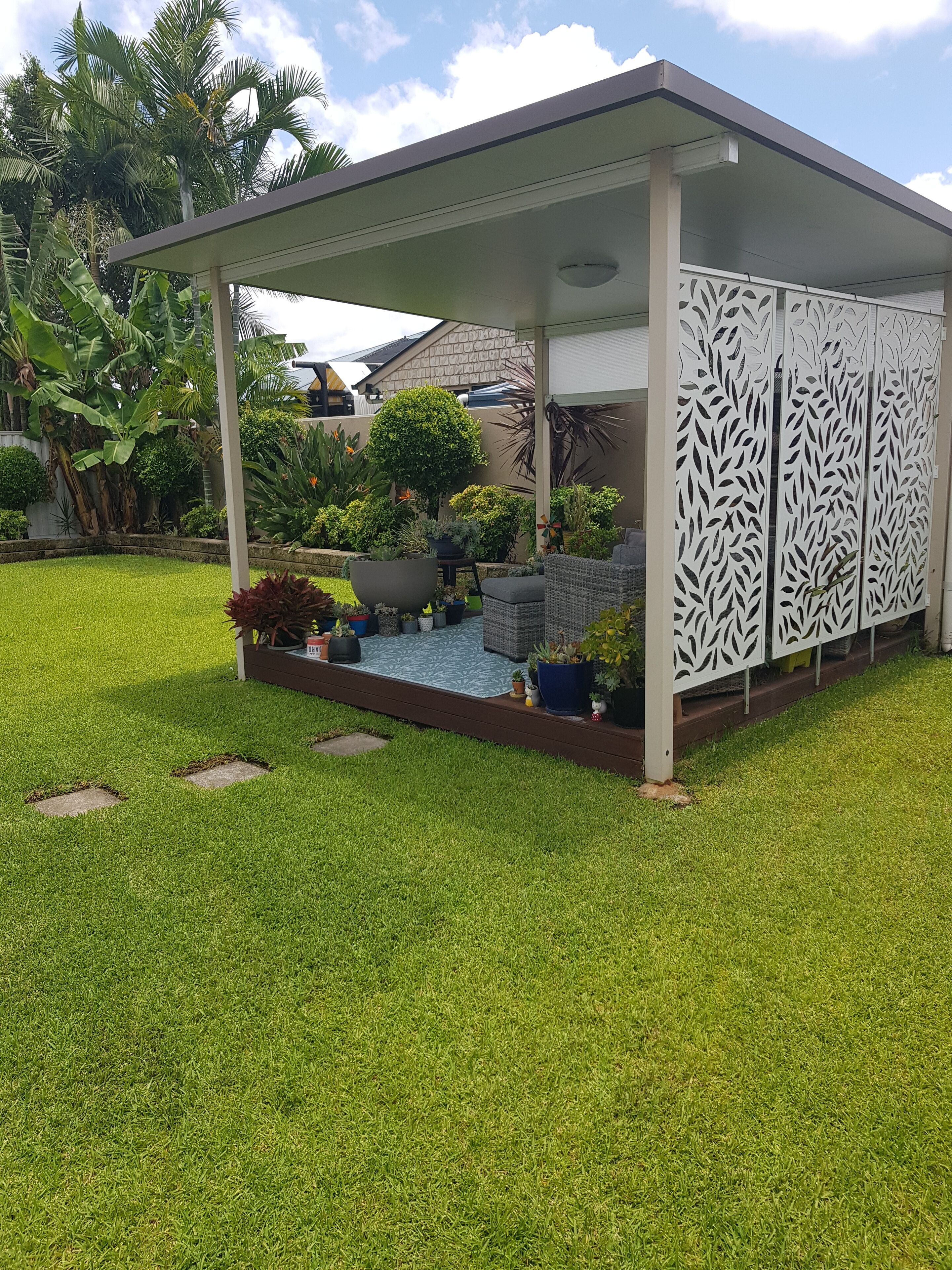 A covered patio area with a decorative white panel, a small water feature, and various potted plants.