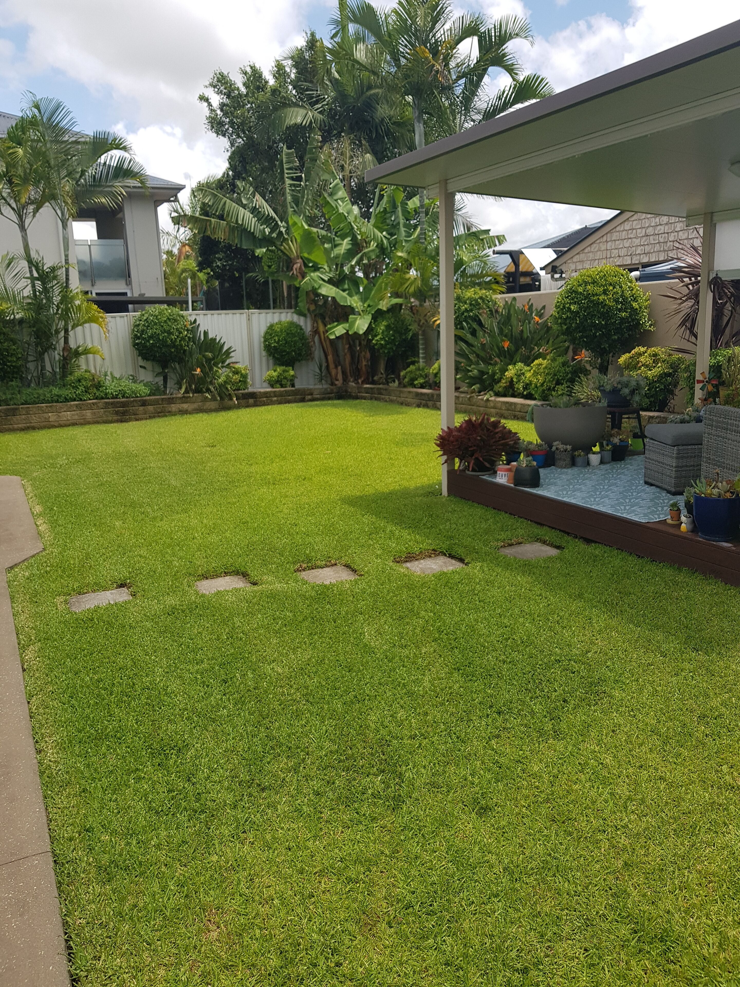A well-maintained lawn with a patio area featuring outdoor furniture and potted plants.