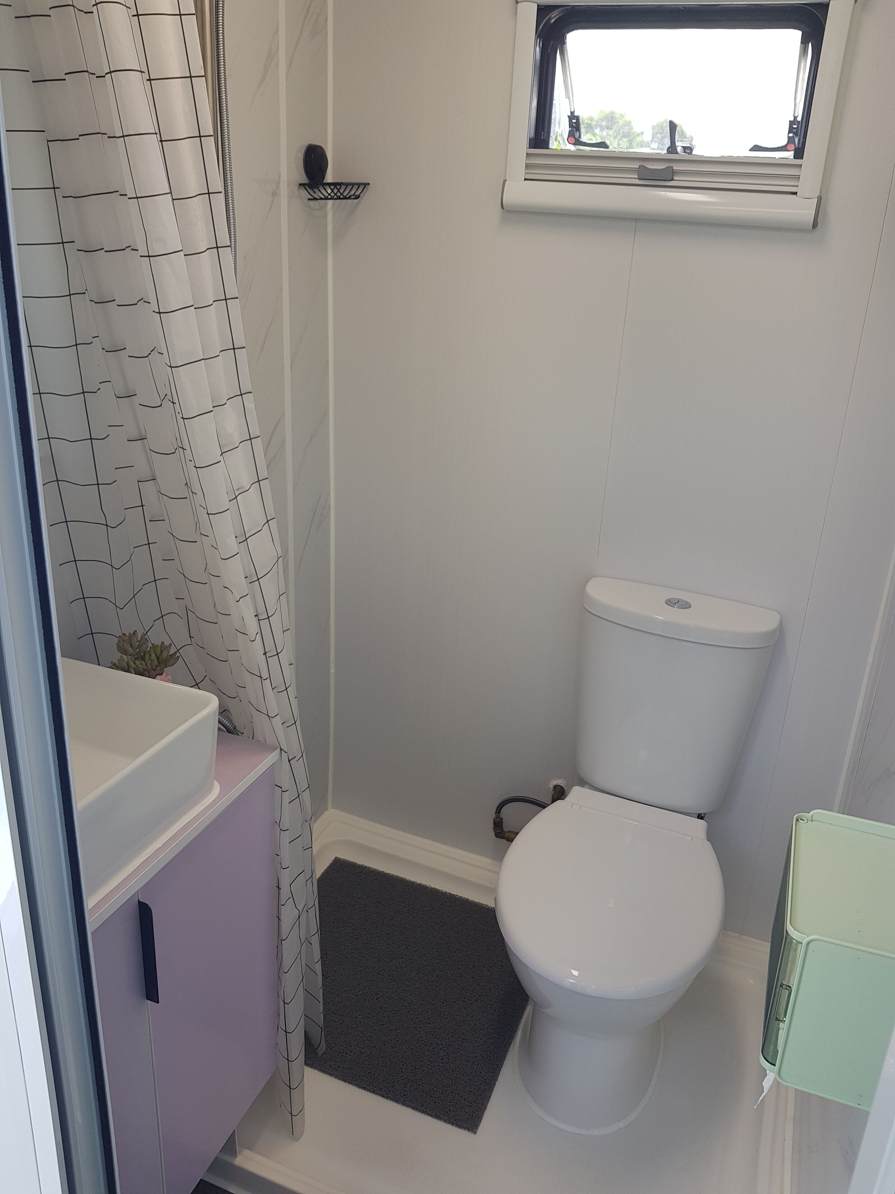 A small bathroom with a toilet, a shower curtain, a window, and a sink.