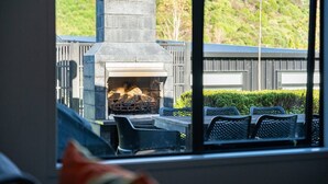 A stone fireplace with a fire burning, surrounded by outdoor furniture. - Riverside in private gated community, with spa pool  & WI-FI, large outdoor area including outdoor , BBQ and alfresco dining, outdoor. Direct access to the river.  Trampoline and ping pong table to keep the  young ( and not so young) entertained. (Taupō)