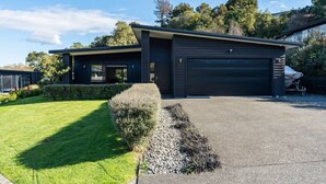 A modern two-story house with a dark exterior, a garage, and a well-maintained lawn. - Riverside in private gated community, with spa pool  & WI-FI, large outdoor area including outdoor , BBQ and alfresco dining, outdoor. Direct access to the river.  Trampoline and ping pong table to keep the  young ( and not so young) entertained. (Taupō)
