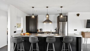 A modern kitchen with a central island, bar stools, pendant lighting, and stainless steel appliances. - Riverside in private gated community, with spa pool  & WI-FI, large outdoor area including outdoor , BBQ and alfresco dining, outdoor. Direct access to the river.  Trampoline and ping pong table to keep the  young ( and not so young) entertained. (Taupō)