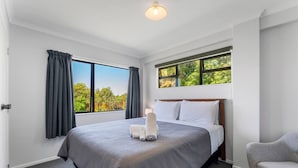 A modern hotel room with a large bed, a view of greenery through the windows, and a small armchair. - Bird Songs and lake views with wifi (Acacia Bay, Taupo)
