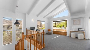 A spacious room with a wooden staircase, a desk with a computer, a comfortable chair, and large windows offering a view of the outdoors. - Bird Songs and lake views with wifi (Acacia Bay, Taupo)