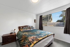 A bedroom with a bed, a nightstand, a window with curtains, and a view of the outside. - Westhall in Kinloch Taupo (Kinloch)