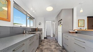 A modern kitchen with grey cabinets, a large island, and a view through the window. - Westhall in Kinloch Taupo (Kinloch)