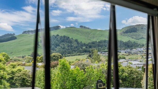 A view of rolling green hills and a residential area through a window with blinds.