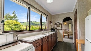 A kitchen with a large window, wooden cabinets, a countertop, and a view of green hills.