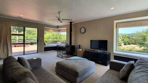 A spacious living room with a large TV, comfortable seating, and a view of the outdoors. - Peaceful on Par Kinloch (Kinloch)