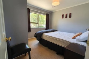 A bedroom with a bed, a window, a door, and a small desk.