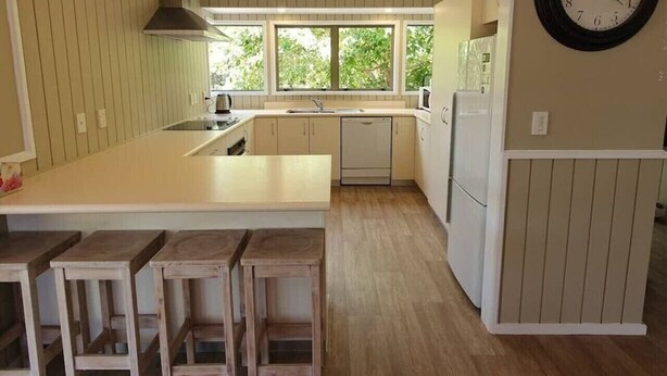 A kitchen with a central island, bar stools, a clock, and a view of greenery outside. - Peaceful on Par Kinloch (Kinloch)
