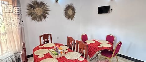 A dining area with a round table covered in a red and white checkered tablecloth, surrounded by wooden chairs.