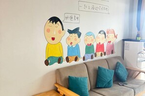 Un soggiorno con divano, cuscini, una parete decorata con un murale di un personaggio dei cartoni animati e un frigorifero.