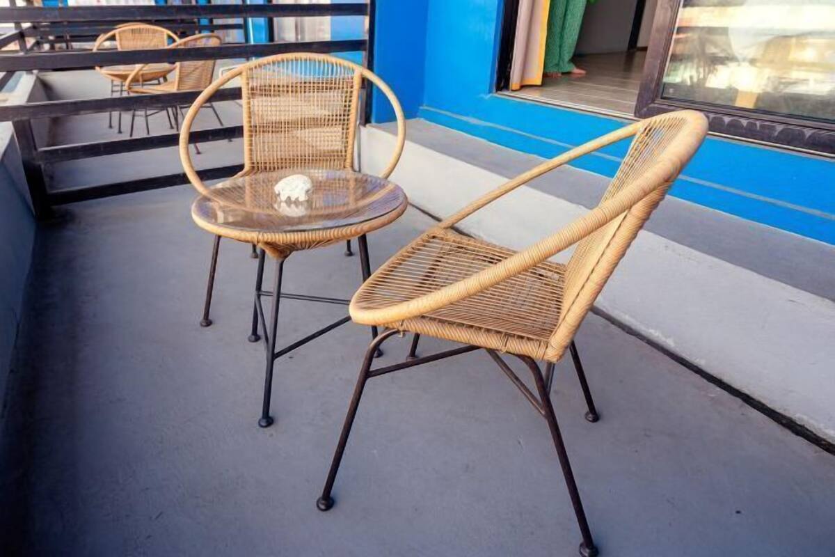 A balcony with wicker chairs and a small round table, a blue wall, and a window with curtains.