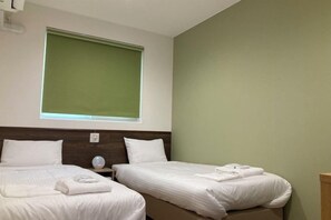 A hotel room with two beds, a window with blinds, a bedside table with a lamp, and a wall-mounted air conditioning unit. - RJ Hotels Otaru (Otaru)