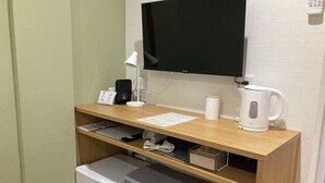 Um espaço de trabalho pequeno com uma mesa, cadeira, televisão, chaleira e um mini-refrigerador.