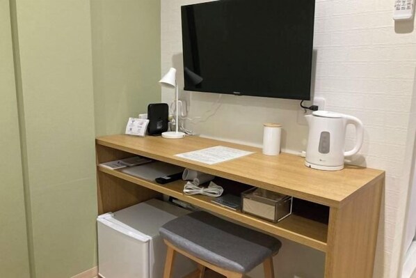 A small workspace with a desk, chair, television, kettle, and a mini-fridge.