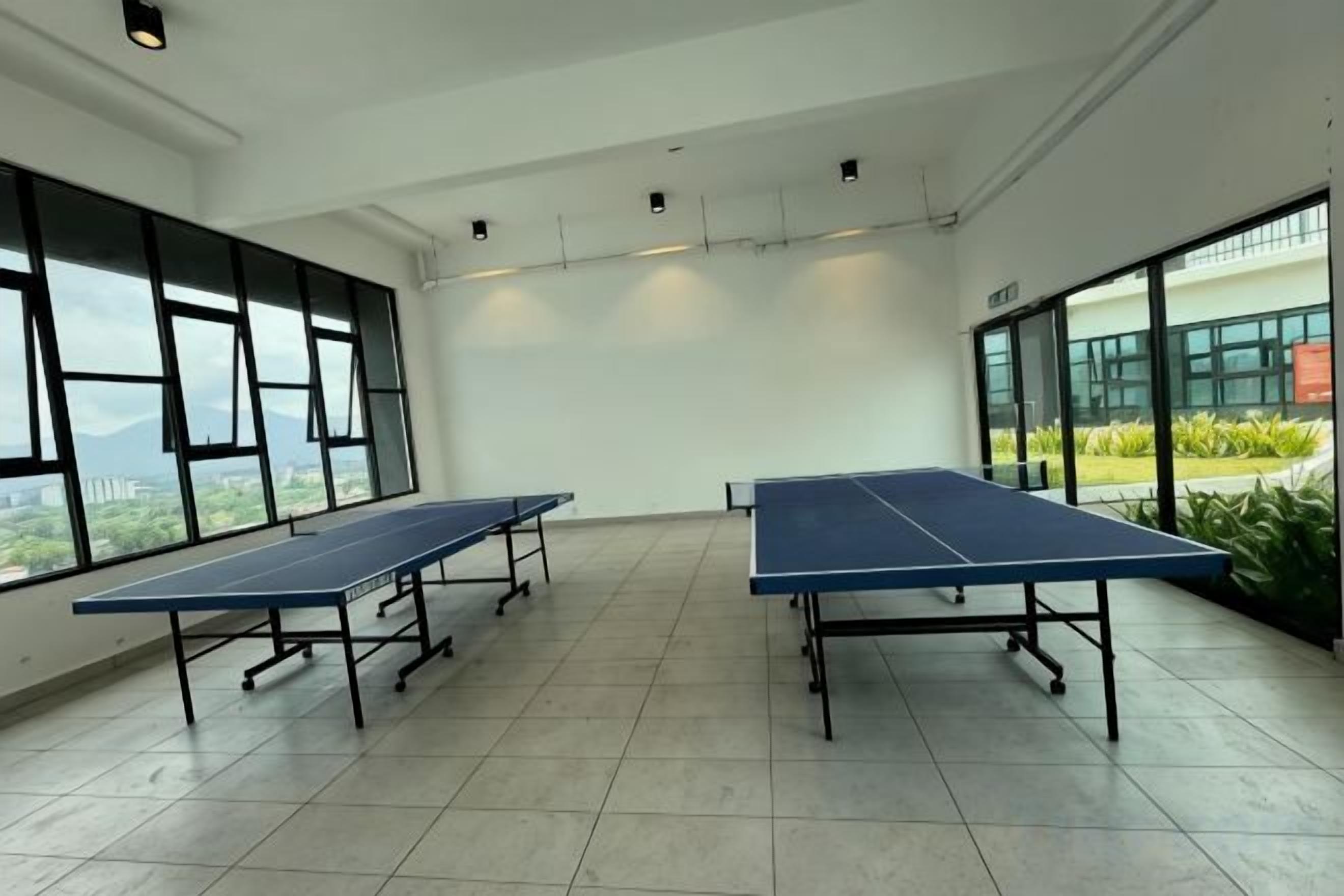 A room with two ping pong tables, large windows, and a view of greenery outside.
