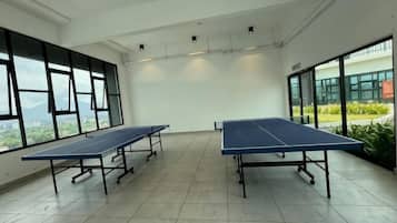 A room with two ping pong tables, large windows, and a view of greenery outside.