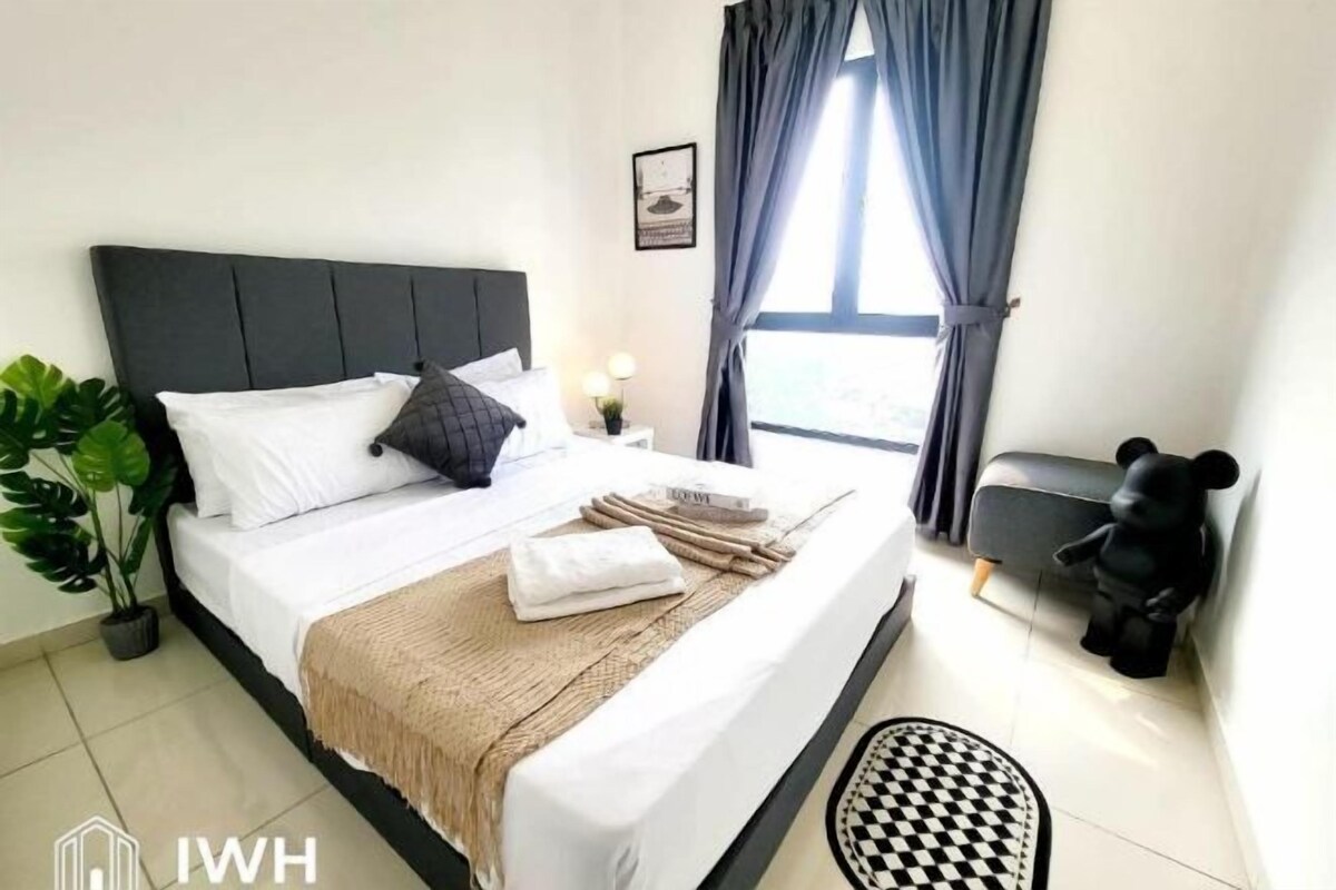 A neatly made bed with white and dark pillows, a beige throw blanket, and a small bedside table with a lamp.