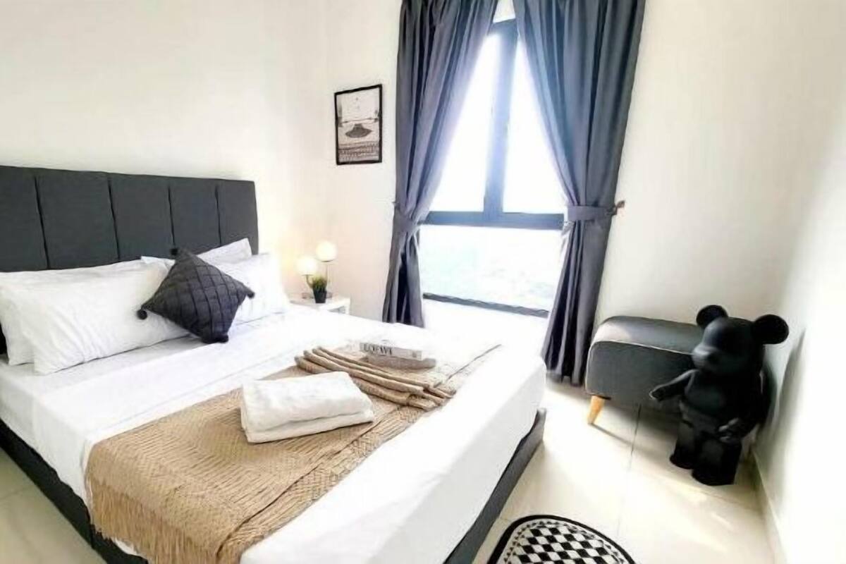 A neatly made bed with white and dark pillows, a beige throw blanket, and a small bedside table with a lamp.