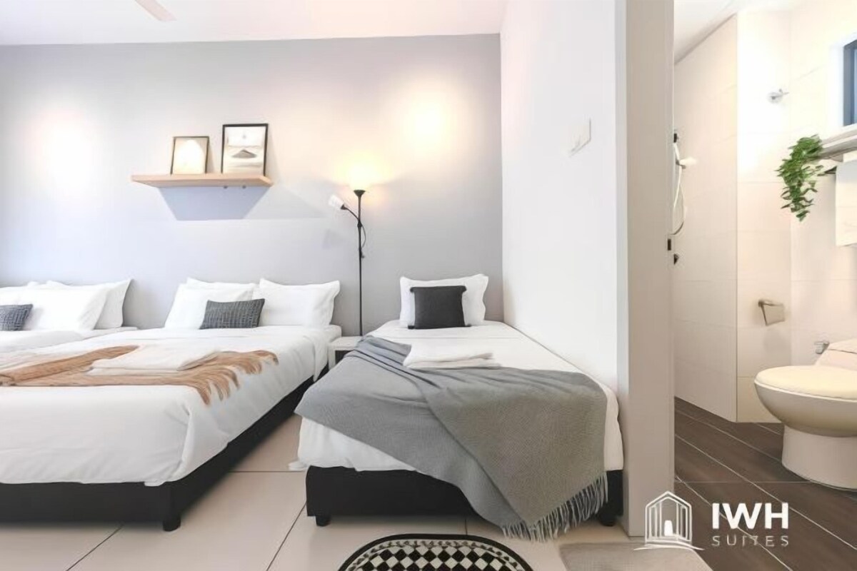 A hotel room with two beds, a bedside table, a lamp, a shelf with pictures, and a bathroom with a toilet and sink.