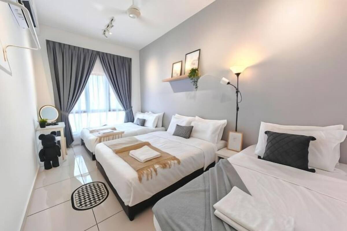 A hotel room with two beds, a bedside table, a lamp, and a window with curtains.