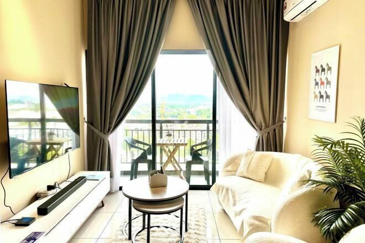 A room with a TV, a small table, a sofa, and a balcony with chairs.
