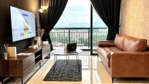 A modern living room with a leather sofa, a flat-screen TV, a small round table, and a view of a construction site through large windows. - Ipoh Town Horizon Skypool Suites 4-11pax by IWH Suites (Ipoh)