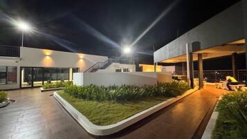 A modern building with a flat roof, a staircase, and a well-lit outdoor area with a paved walkway and greenery.