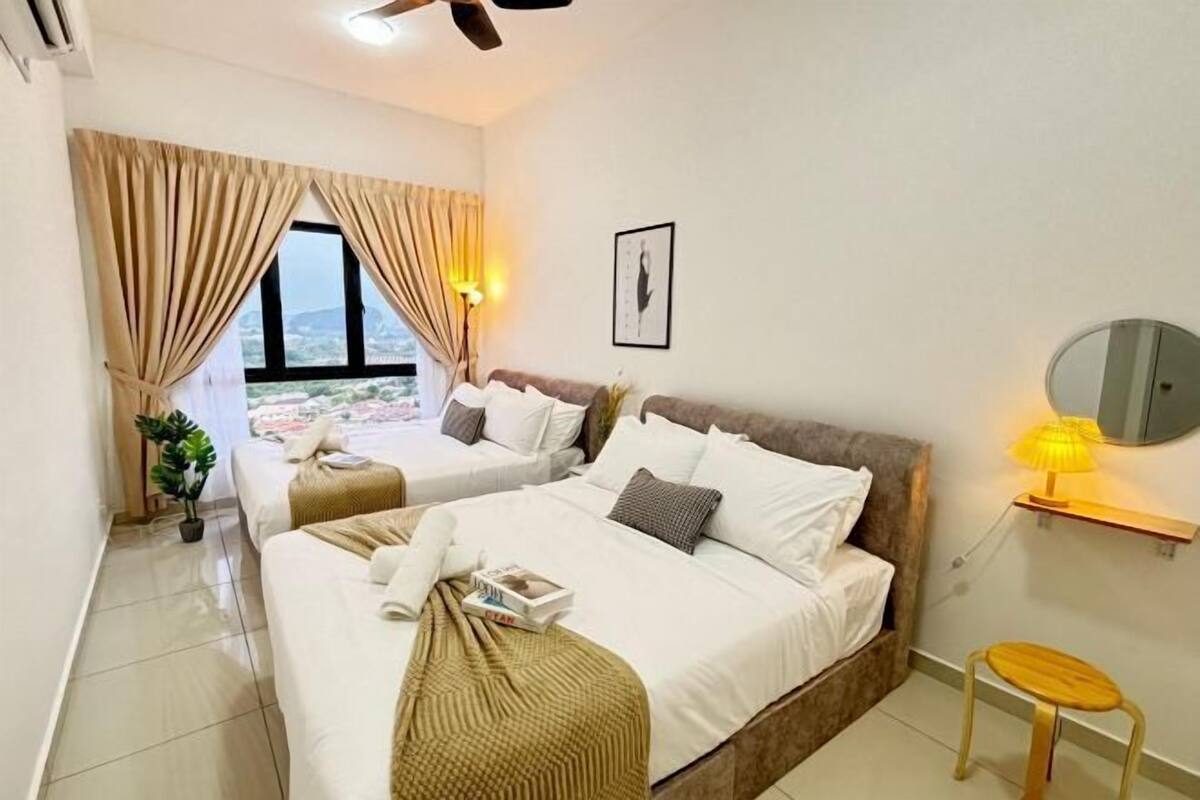 A hotel room with two beds, a window with curtains, a bedside lamp, a small table, and a framed picture on the wall.