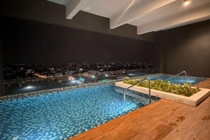 Une piscine intérieure offrant une vue sur le paysage urbain illuminé la nuit.