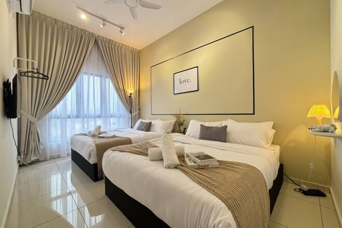 A hotel room with two beds, a large framed 'love' sign on the wall, and a view of the outdoors through the window.