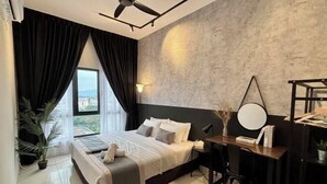 A modern bedroom with a bed, a desk, a chair, a potted plant, and a view of the city through a large window. - Ipoh Town Horizon Skypool Suites 4-11pax by IWH Suites (Ipoh)