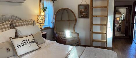 A bedroom with a bed, a ladder, a chair, and a painting on the wall.