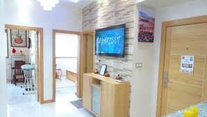 A modern hotel room with a wooden reception desk, a flat-screen TV, a bed, a dining area, and a bathroom. - Paradise House Apartment in Tamraght (Tamraght)