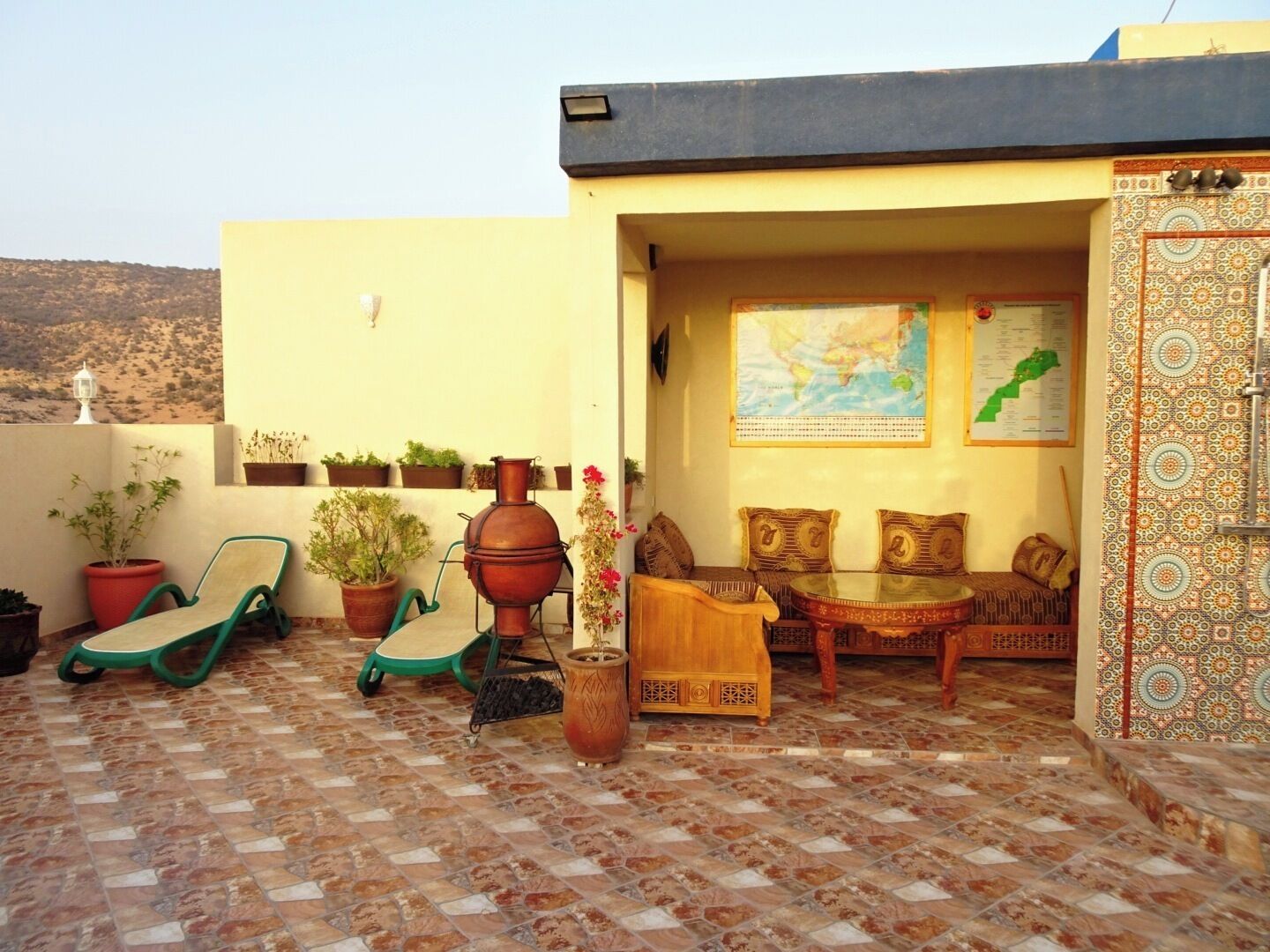 A rooftop terrace with a seating area, potted plants, and a decorative wall.