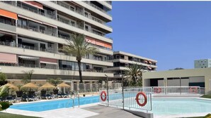 Un hotel de varios pisos con piscina, palmeras y sillones de descanso.