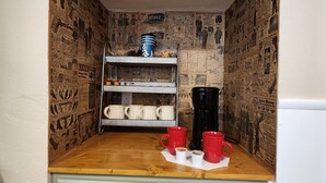 Een kleine kitchenette met een houten aanrecht, een koffiezetapparaat en een plank met mokken.