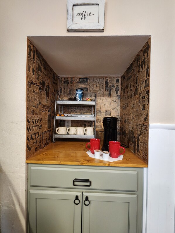 Una kitchenette pequeña con cubierta de madera, una cafetera y una repisa con tazas.