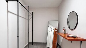 Un pasillo con un perchero metálico, un armario blanco, una estantería de madera con un espejo y suelo de baldosas grises.