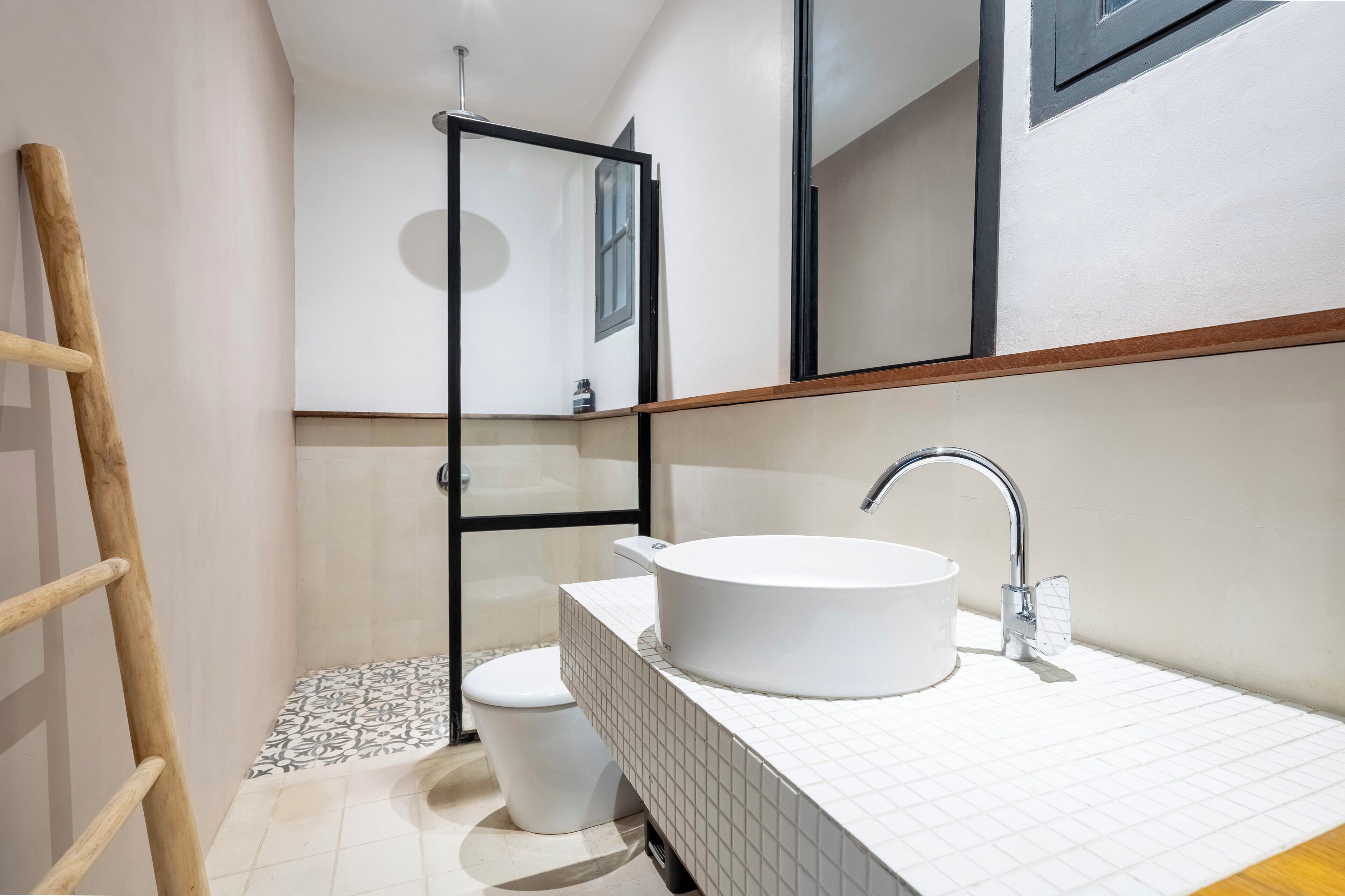 A modern bathroom with a white sink, a glass shower enclosure, and a wooden ladder.