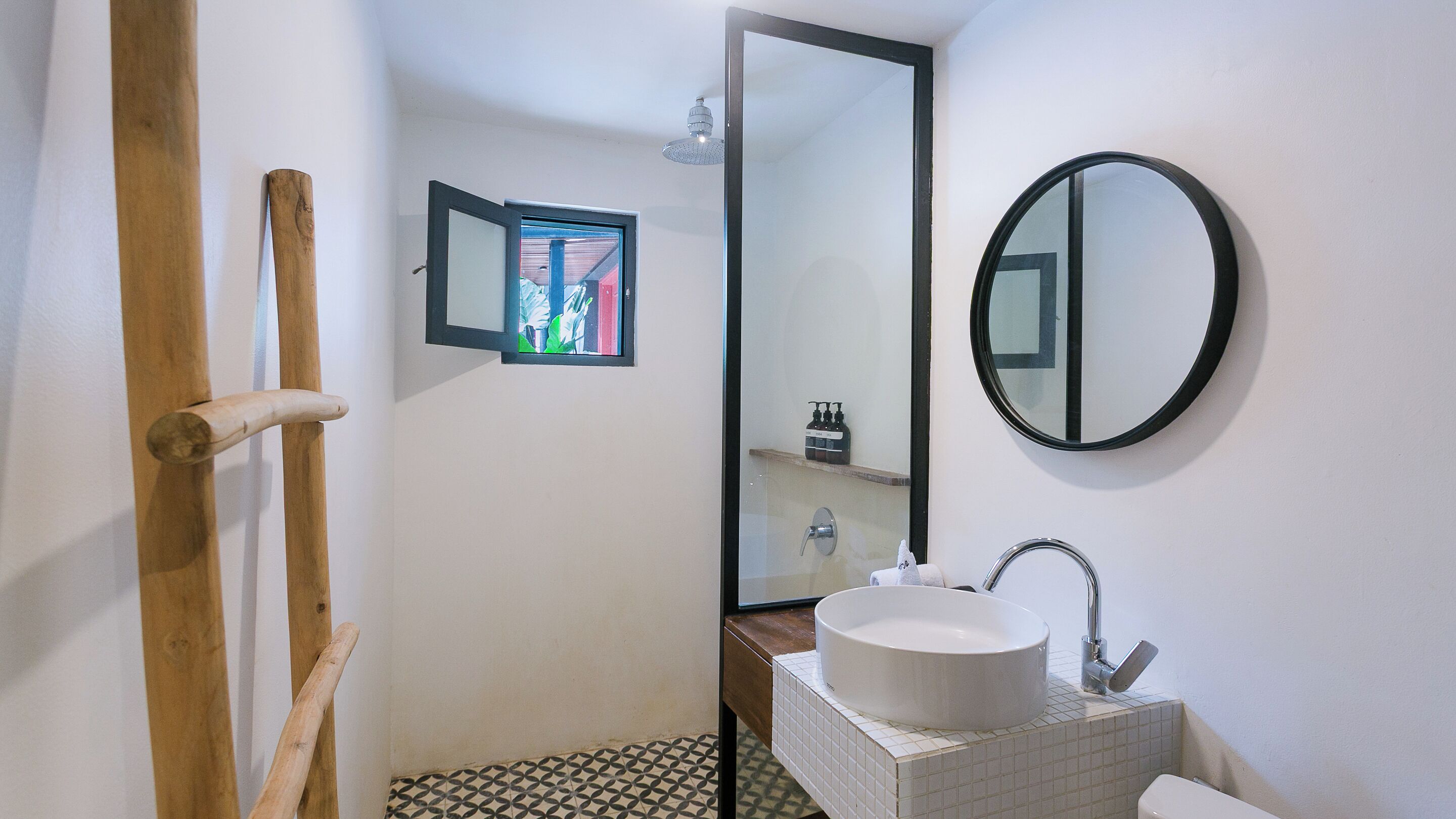 A bathroom with a wooden door, a white sink, a mirror, and a tiled floor.