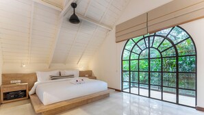 A bedroom with a large arched window, a wooden bed, and a nightstand with a radio. - Bon Ton Villa By Betterplace (Canggu)