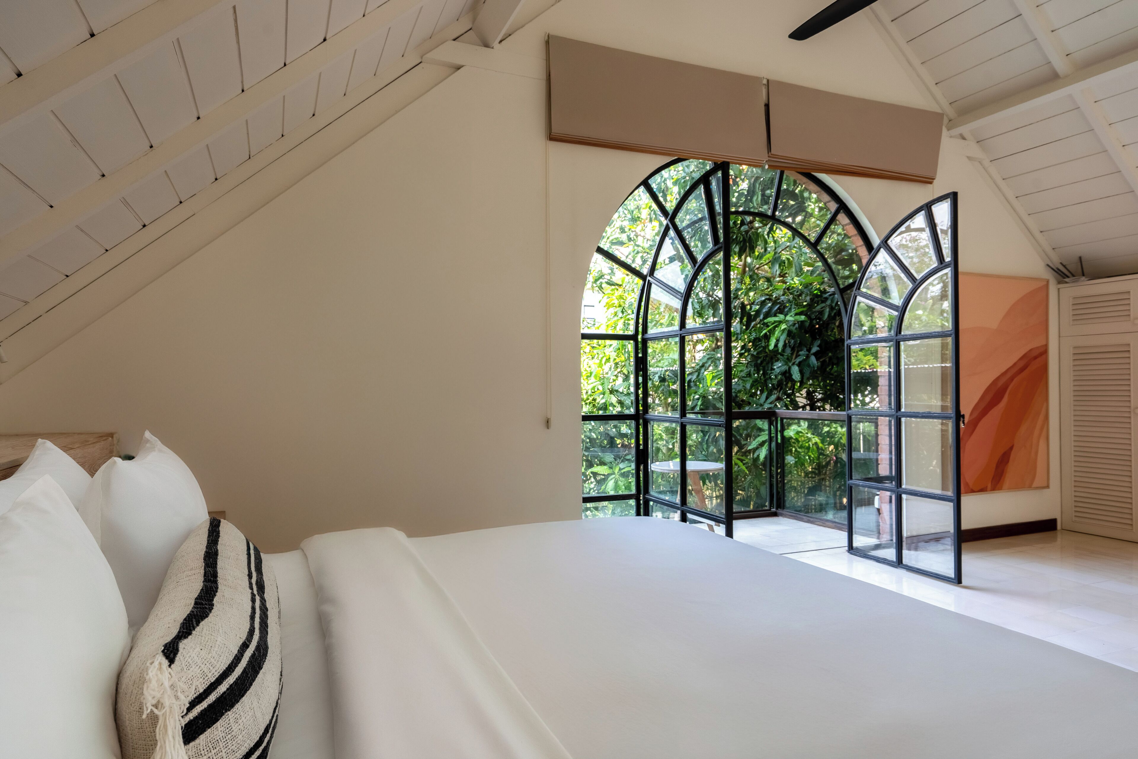 A bedroom with a large bed, a window with a view of greenery, and a ceiling fan.
