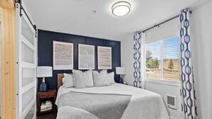 A bedroom with a bed, two bedside tables, a window with curtains, and artwork on the wall. - Library INN LLC (Lava Hot Springs)