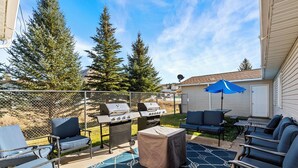 An outdoor patio with a grill, chairs, and a covered table. - Library INN LLC (Lava Hot Springs)