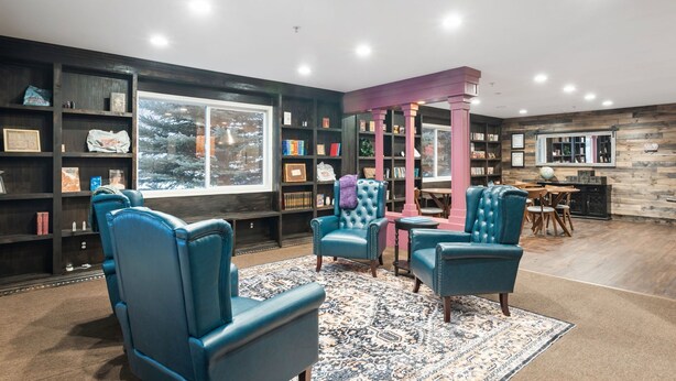 A cozy reading area with leather chairs, a large bookshelf, and a window with a view of trees. - Library INN LLC (Lava Hot Springs)