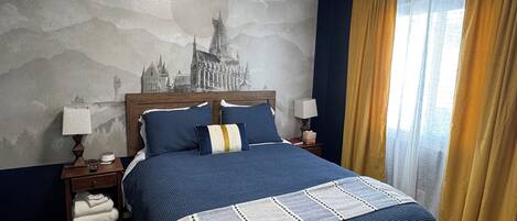Habitación de hotel con una cama grande, una mesita de noche, una lámpara, un mural en la pared y una ventana con cortinas.